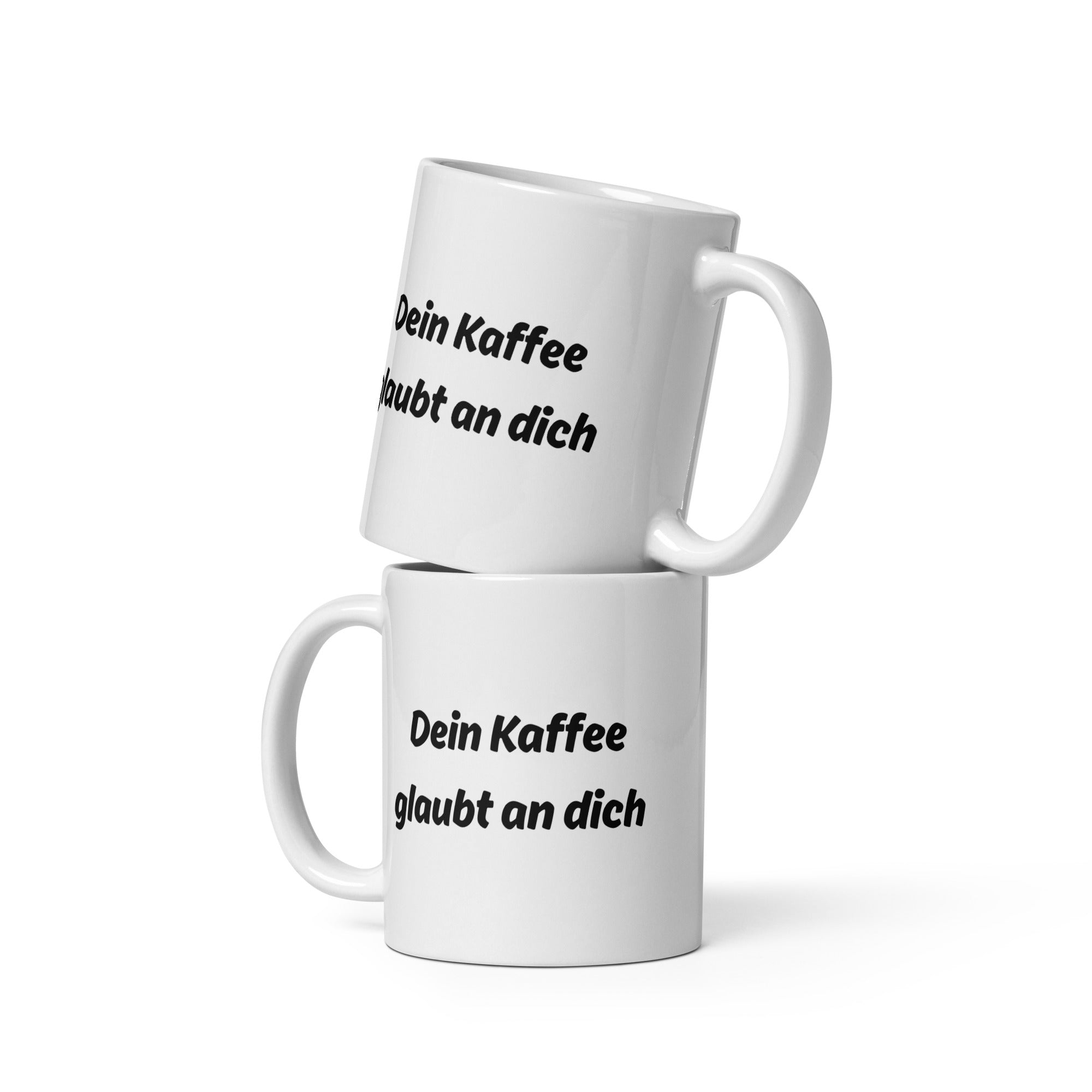 Zwei weiße Kaffeetassen mit schwarzem Schriftzug ‚Dein Kaffee glaubt an dich‘, übereinander gestapelt.