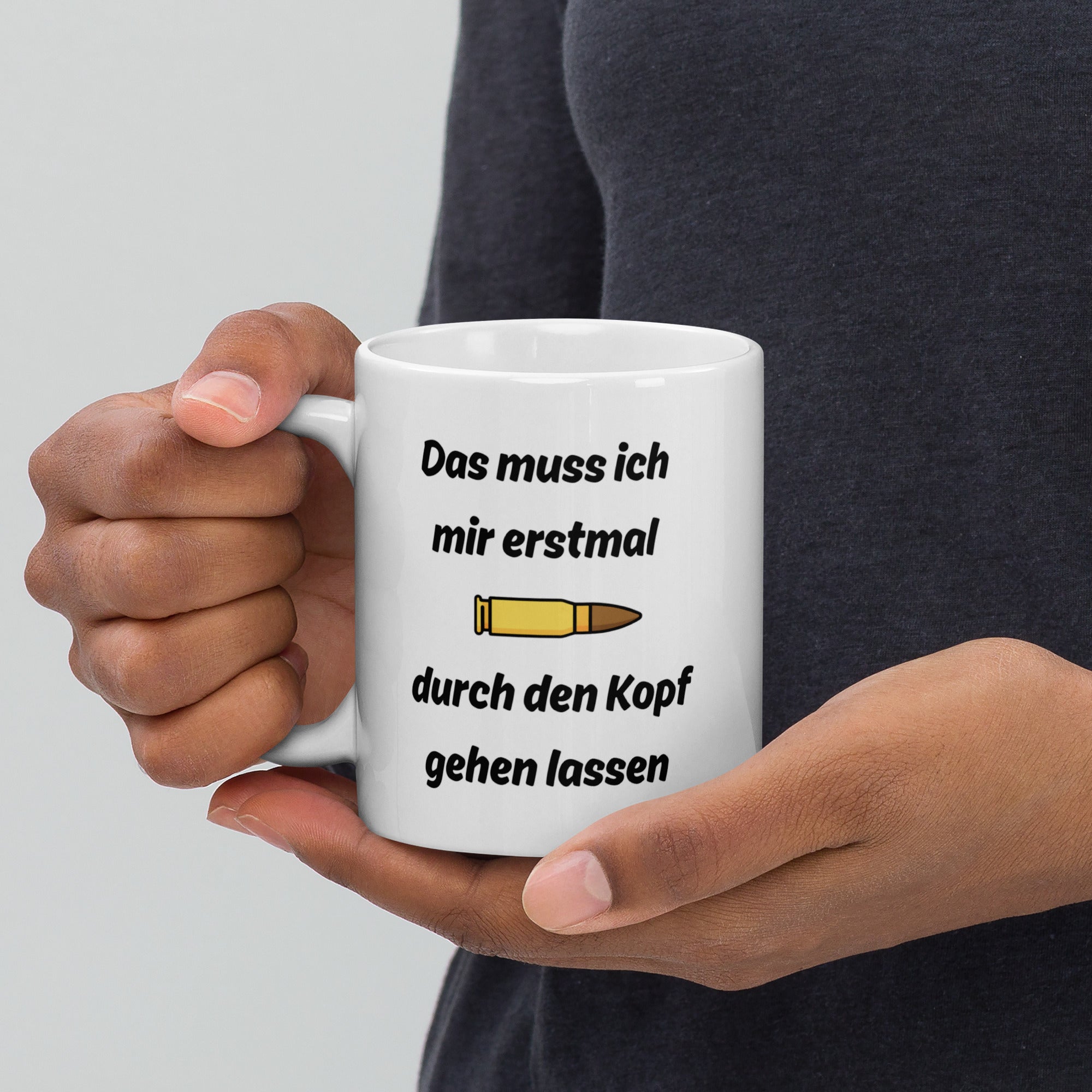 Eine Hand hält eine weiße Kaffeetasse mit Patronen-Motiv und schwarzem Spruch ‚Das muss ich mir erst mal durch den Kopf gehen lassen‘.
