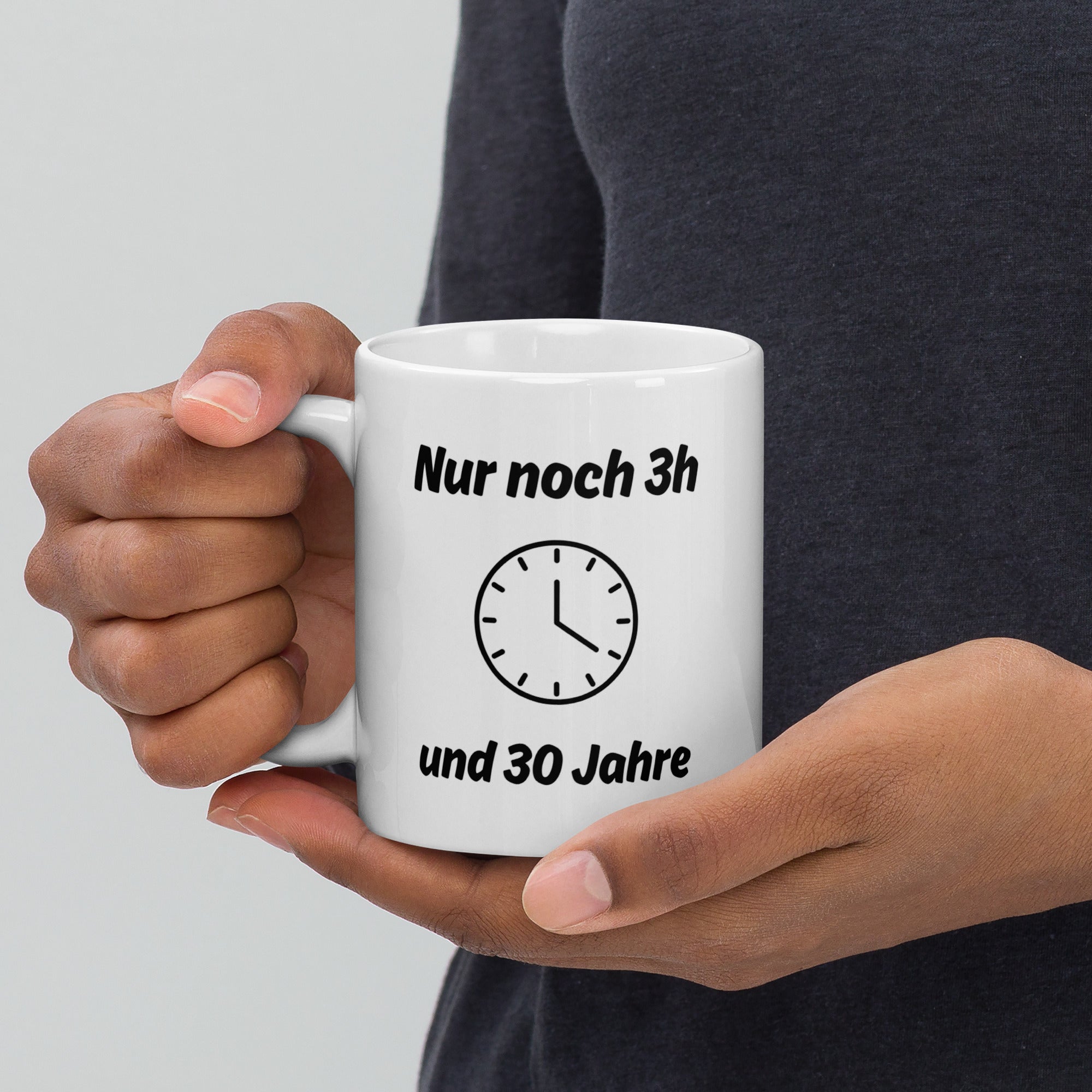 Eine Hand hält eine weiße Kaffeetasse mit Uhr-Motiv und schwarzem Spruch ‚Nur noch 3h und 30 Jahre‘.