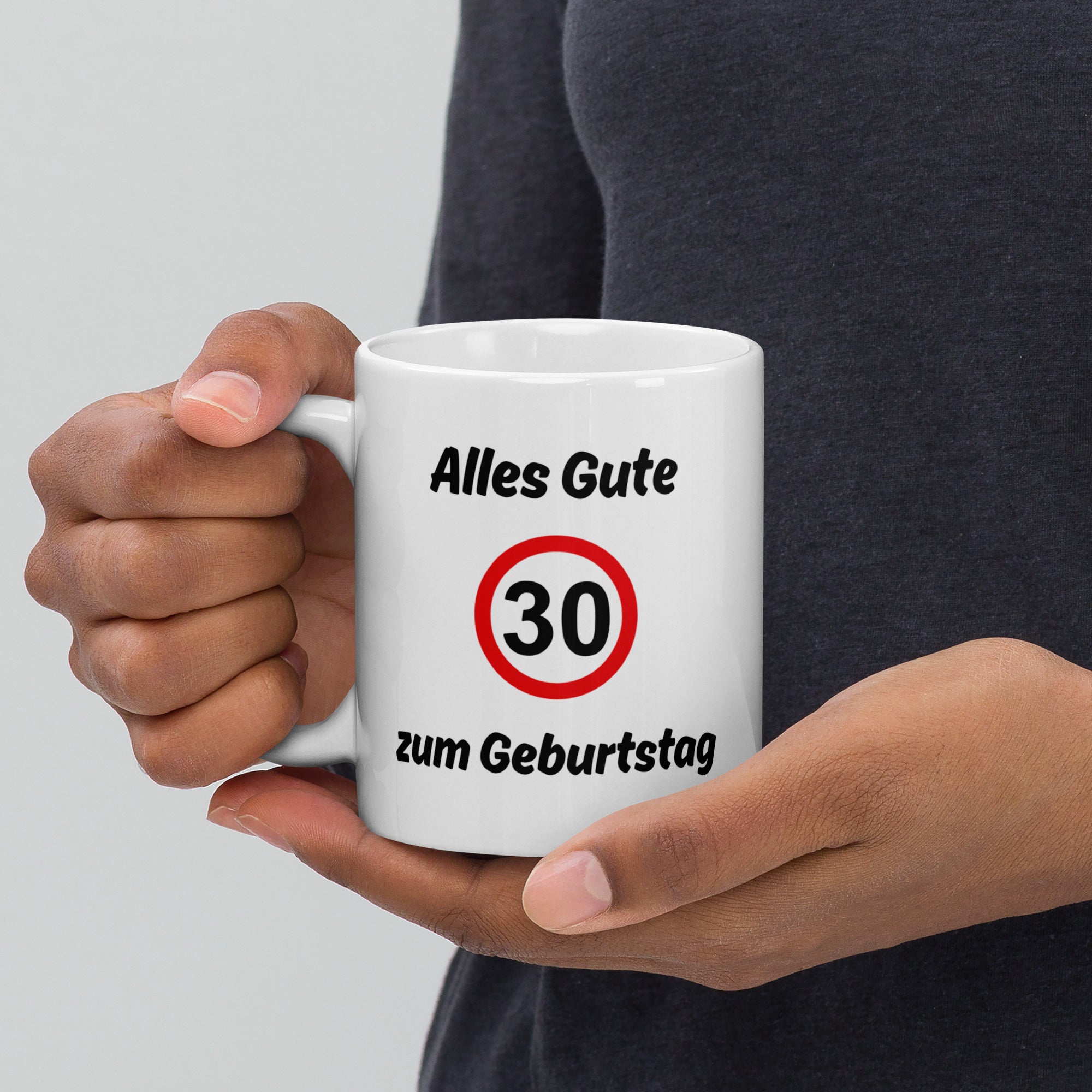 Eine Hand hält eine weiße Kaffeetasse mit Spruch ‚Alles Gute zum Geburtstag‘ und rotem Verkehrszeichen mit der Zahl 30.