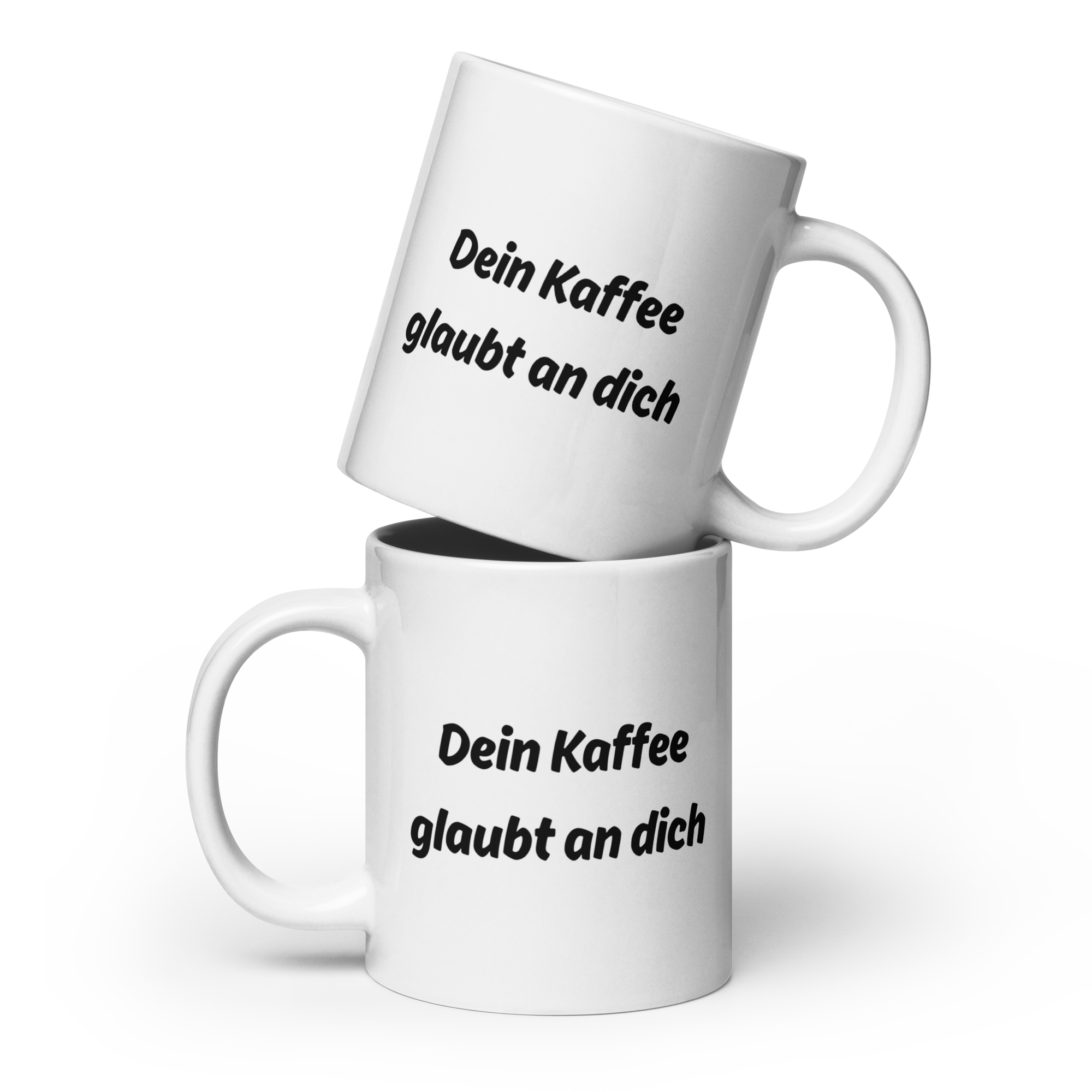 Zwei weiße Kaffeetassen mit schwarzem Spruch-Aufdruck ‚Dein Kaffee glaubt an dich‘, übereinandergestapelt.