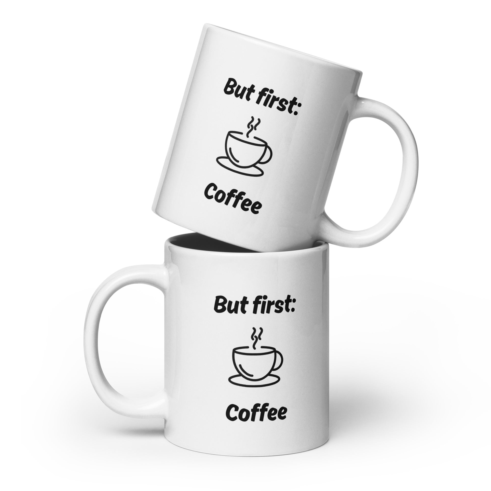 Zwei weiße Kaffeetassen mit schwarzer Aufschrift ‚But first: Coffee‘ und Illustration einer dampfenden Kaffeetasse, übereinandergestapelt.